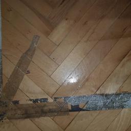 Sanpa Sp. z o.o. - Parkiet w jodełkę z pozostałościami kleju i taśmy malarskiej po remoncie, widoczne ślady po usunięciu zabezpieczeń.