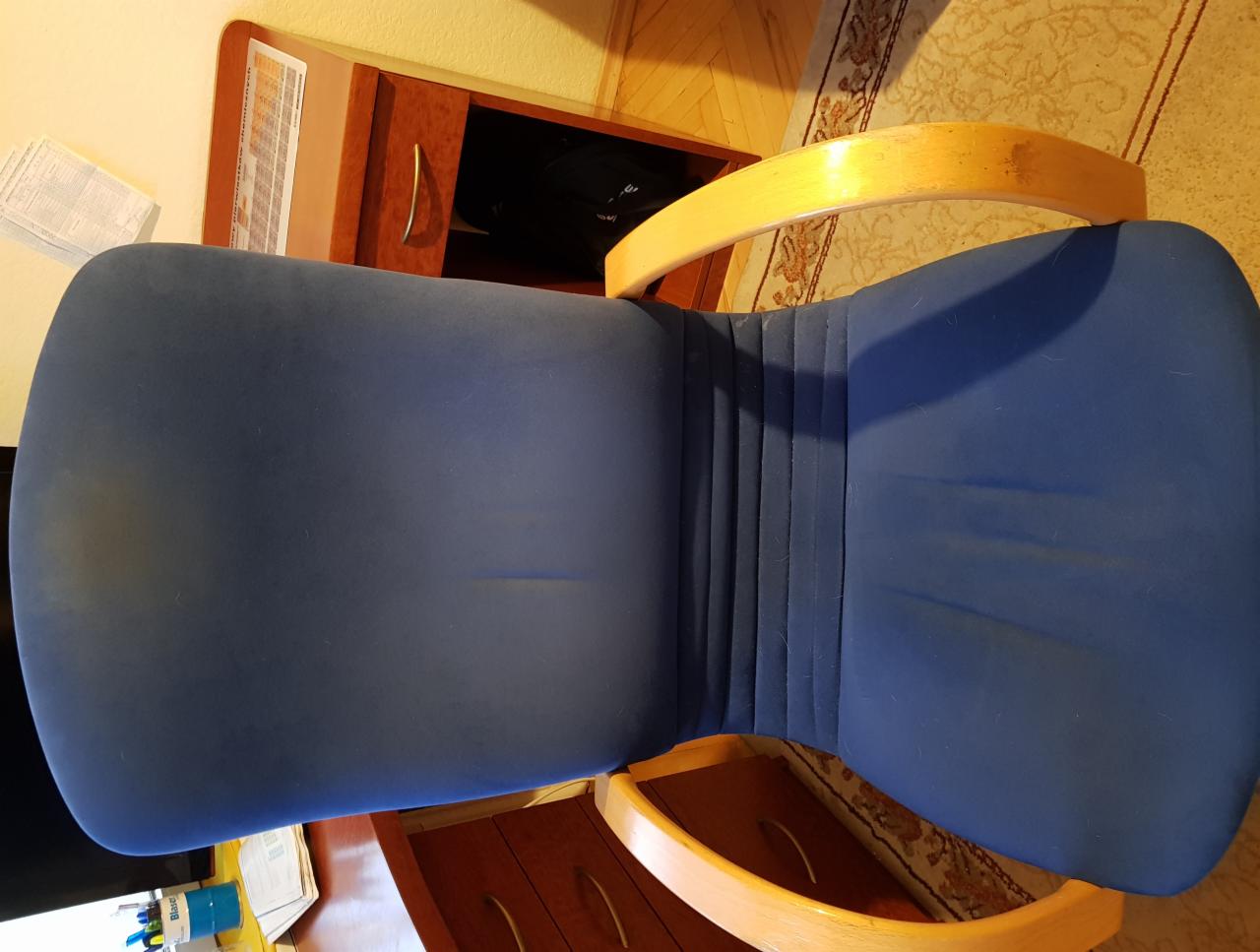 Niebieskie krzesło biurowe z drewnianymi podłokietnikami widziane z góry, na siedzisku widoczne lekkie odbarwienia.