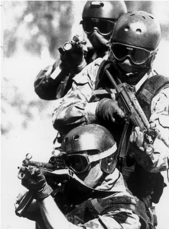 Czarno-białe zdjęcie trzech uzbrojonych mężczyzn w hełmach i goglach, z karabinami, w trakcie ćwiczeń lub akcji.