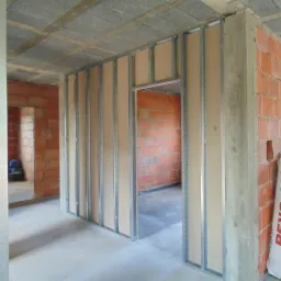 Montaż ścian działowych z płyty karton gips na metalowym stelażu w surowym wnętrzu z ceglanymi ścianami, widoczny worek z wełną mineralną Ursa.