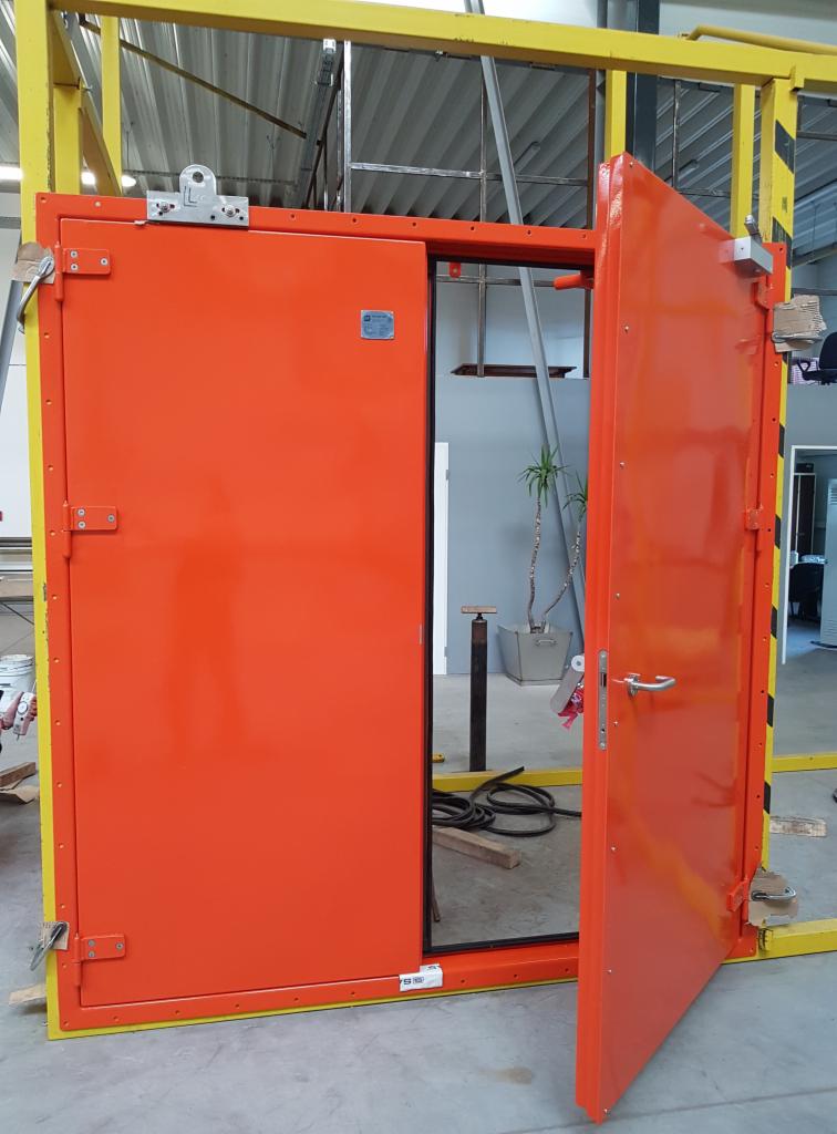 Pomarańczowe, przesuwne drzwi przemysłowe zamontowane przez firmę z Niepruszewa, widoczne w częściowym otwarciu, z metalową konstrukcją ramy w kolorze żółtym i czarnym.