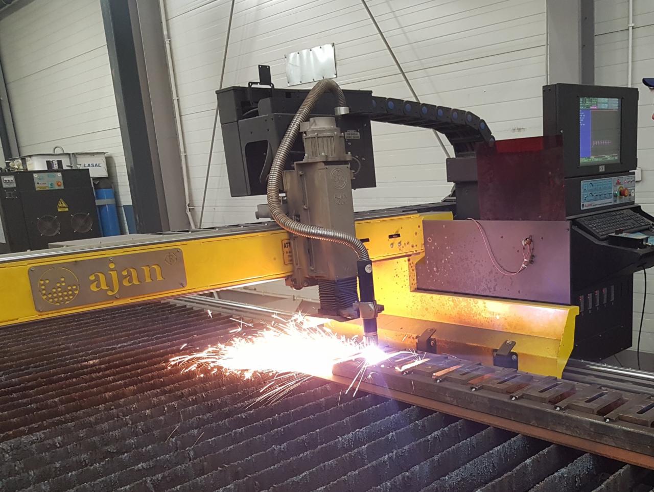 Żółto-czarna maszyna CNC marki Ajan w trakcie cięcia metalu, z widocznymi iskrami i ekranem sterującym po prawej stronie.