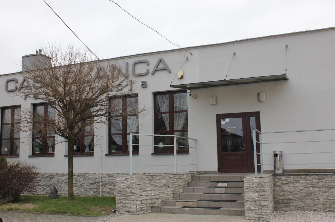 Fasada budynku z napisem 'Casablanca' nad oknami, widoczne schody wejściowe i drzewo bez liści przed budynkiem.