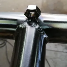 Szczeg&oacute;łowe zbliżenie spawu łączącego rury konstrukcyjne z nakrętką, widoczne ślady obr&oacute;bki i charakterystyczne przebarwienia termiczne metalu.