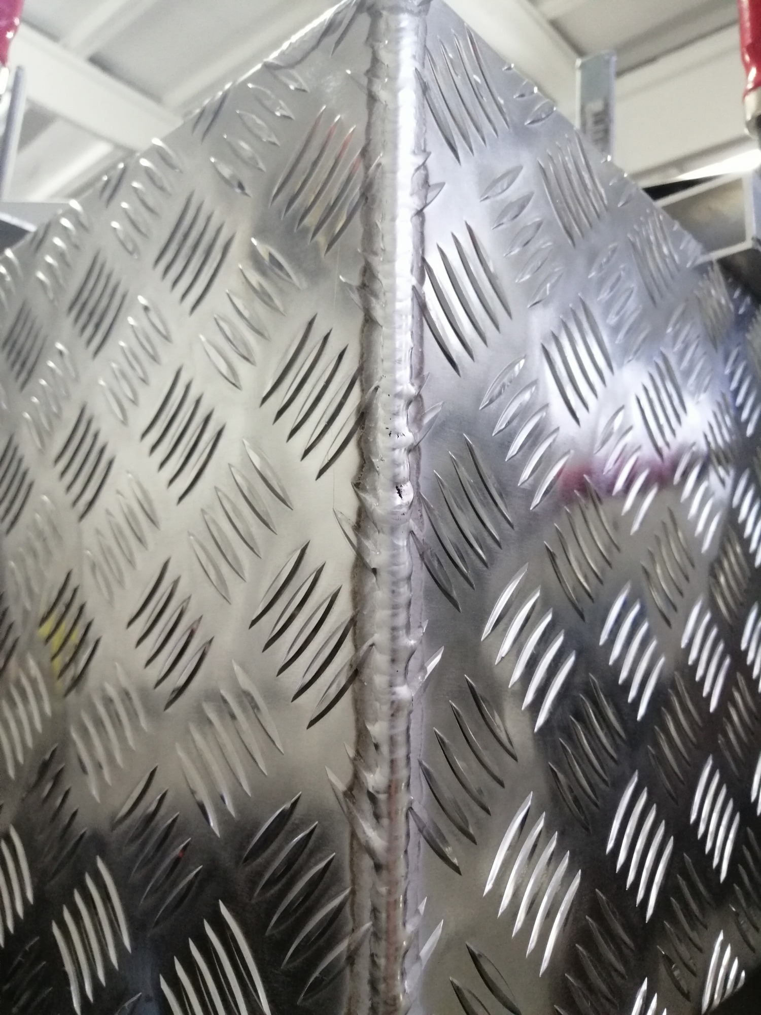 Fragment spawanej konstrukcji z blachy aluminiowej o antypoślizgowej fakturze, widoczny szew spawalniczy.