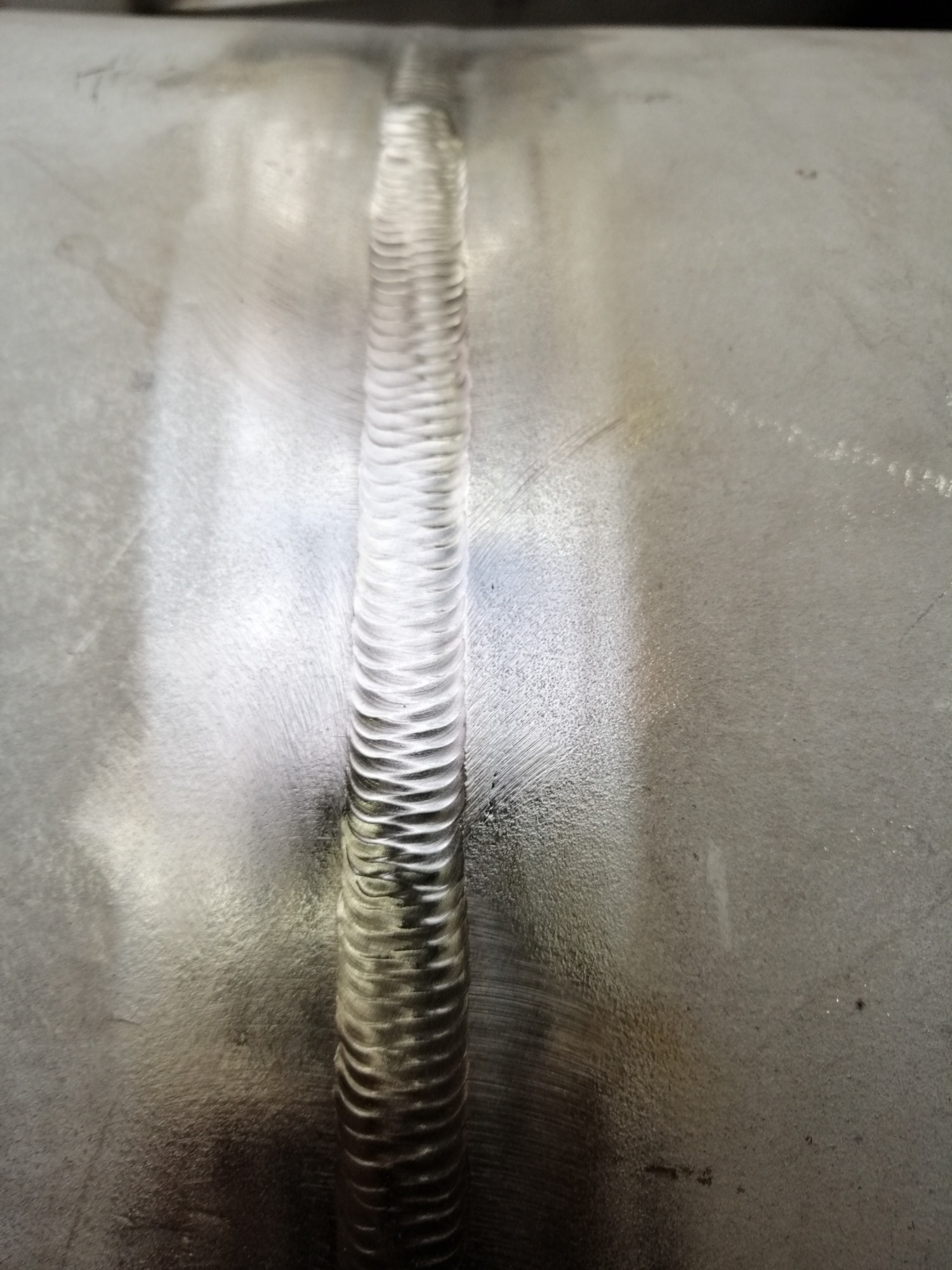 Szlifowana powierzchnia metalu ze świeżym, regularnym spawem w centralnej części kadru.