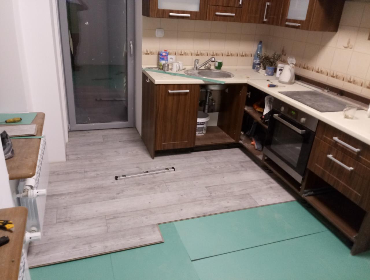 W trakcie prac: podłoga w kuchni w Zielonej Górze z częściowo ułożonymi panelami na zielonym podkładzie. Widoczna poziomica i narzędzia.