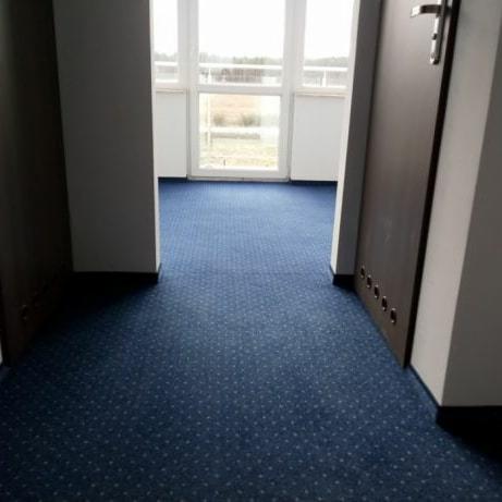 Granatowa wykładzina dywanowa z drobnym wzorem w korytarzu, widok na okno balkonowe z odległym krajobrazem.