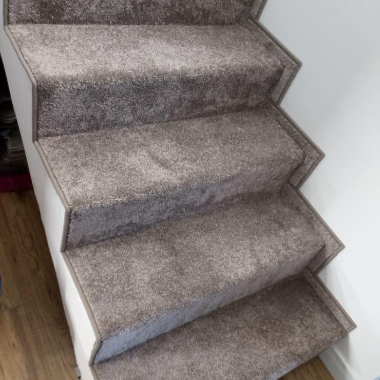 Schody obite szarą wykładziną dywanową, widok z dołu, z delikatnym brązowym akcentem na krawędziach stopni.