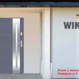 Nowoczesne, grafitowe drzwi wejściowe z pionowym, srebrnym panelem, zamontowane w jasnym budynku, obok widoczny plakat reklamowy marki WIKĘD z informacjami o konstrukcji i wyposażeniu drzwi.