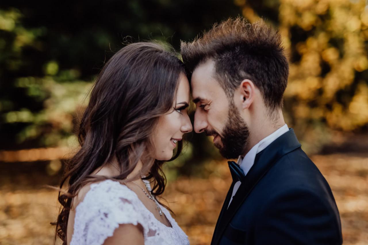 Zakochana para z Wrocławia, zbliżona twarzami w plenerze, ona w białej sukni z koronką, on w granatowym garniturze z muszką, delikatne oświetlenie podkreśla emocje.