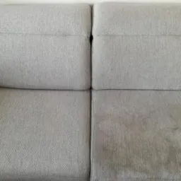 Fragment szarej kanapy: po lewej stronie widoczna czysta powierzchnia, po prawej zabrudzona, ukazująca efekt przed i po zabiegu.