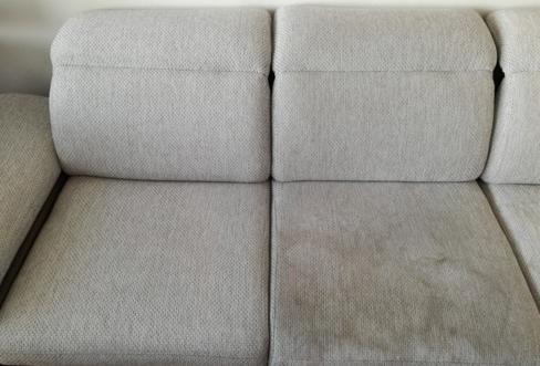 Fragment szarej kanapy: po lewej stronie widoczna czysta powierzchnia, po prawej zabrudzona, ukazująca efekt przed i po zabiegu.