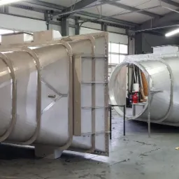 Dwie duże, metalowe konstrukcje o przekroju okrągłym i kwadratowym w hali w Sielecu, prawdopodobnie elementy instalacji wentylacyjnej lub przemysłowej, w trakcie montażu lub przygotowania...