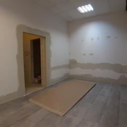 M.S. Vel-BUD Firma Rodzinna - Przygotowanie do montażu płyt karton gips na ścianach w surowym wnętrzu. Widoczne płyty na podłodze, ślady szpachlowania na ścianach i otwarte przejście do innego pomieszczenia.