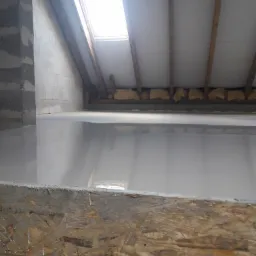 Poddasze po wylaniu posadzki samopoziomującej, widoczne okno dachowe i ocieplenie między krokwiami.