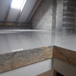 M.S. Vel-BUD Firma Rodzinna - Wylewka samopoziomująca na poddaszu z oknem dachowym, widoczne bloczki betonowe na ścianach i drewniana konstrukcja dachu.