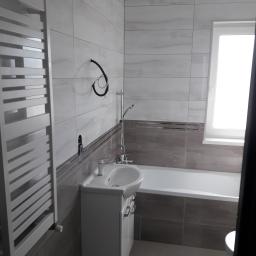 M.S. Vel-BUD Firma Rodzinna - Wykończona łazienka z wanną, umywalką z szafką i grzejnikiem drabinkowym, widoczne przyłącza instalacyjne przed wykończeniem.