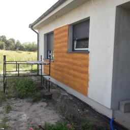 M.S. Vel-BUD Firma Rodzinna - Montaż paneli imitujących drewno na elewacji domu jednorodzinnego, widoczne rusztowanie i niedokończone prace wykończeniowe.
