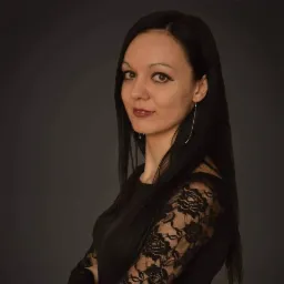 Portret kobiety z długimi czarnymi włosami, ubranej w czarną sukienkę z koronkowymi rękawami na ciemnoszarym tle.