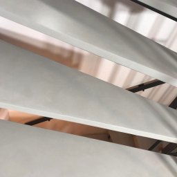 Mkcement - Szare, poziome panele z czarnymi elementami konstrukcyjnymi, ułożone pod kątem, widok z dołu.