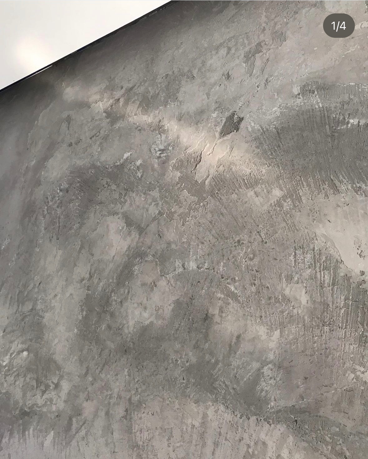 Szara ściana z efektem betonu architektonicznego, widoczne ślady po pacy i nierównomierna faktura, oświetlenie górne.