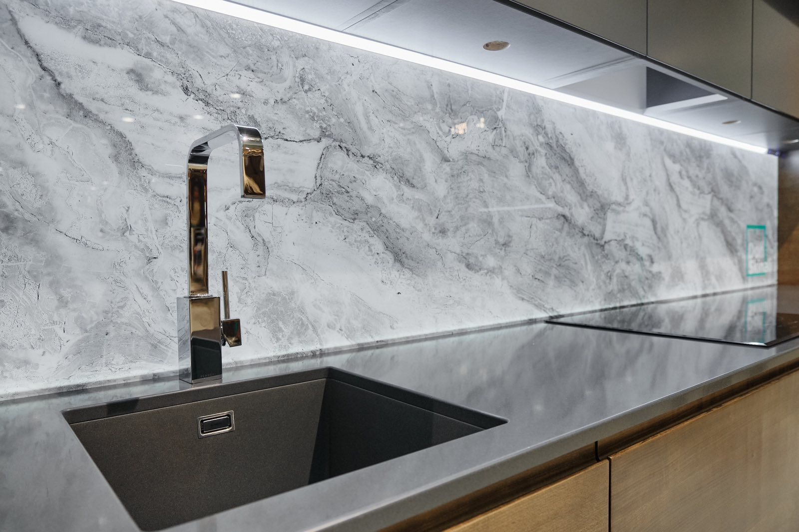 Nowoczesna kuchnia z marmurowym panelem ściennym, chromowaną baterią i minimalistycznym, grafitowym zlewem podblatowym.