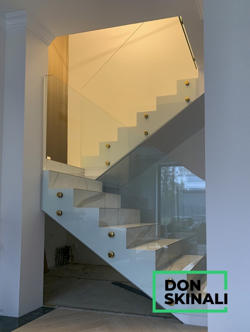Nowoczesna balustrada szklana na marmurowych schodach z złotymi mocowaniami, widok z dołu schodów.