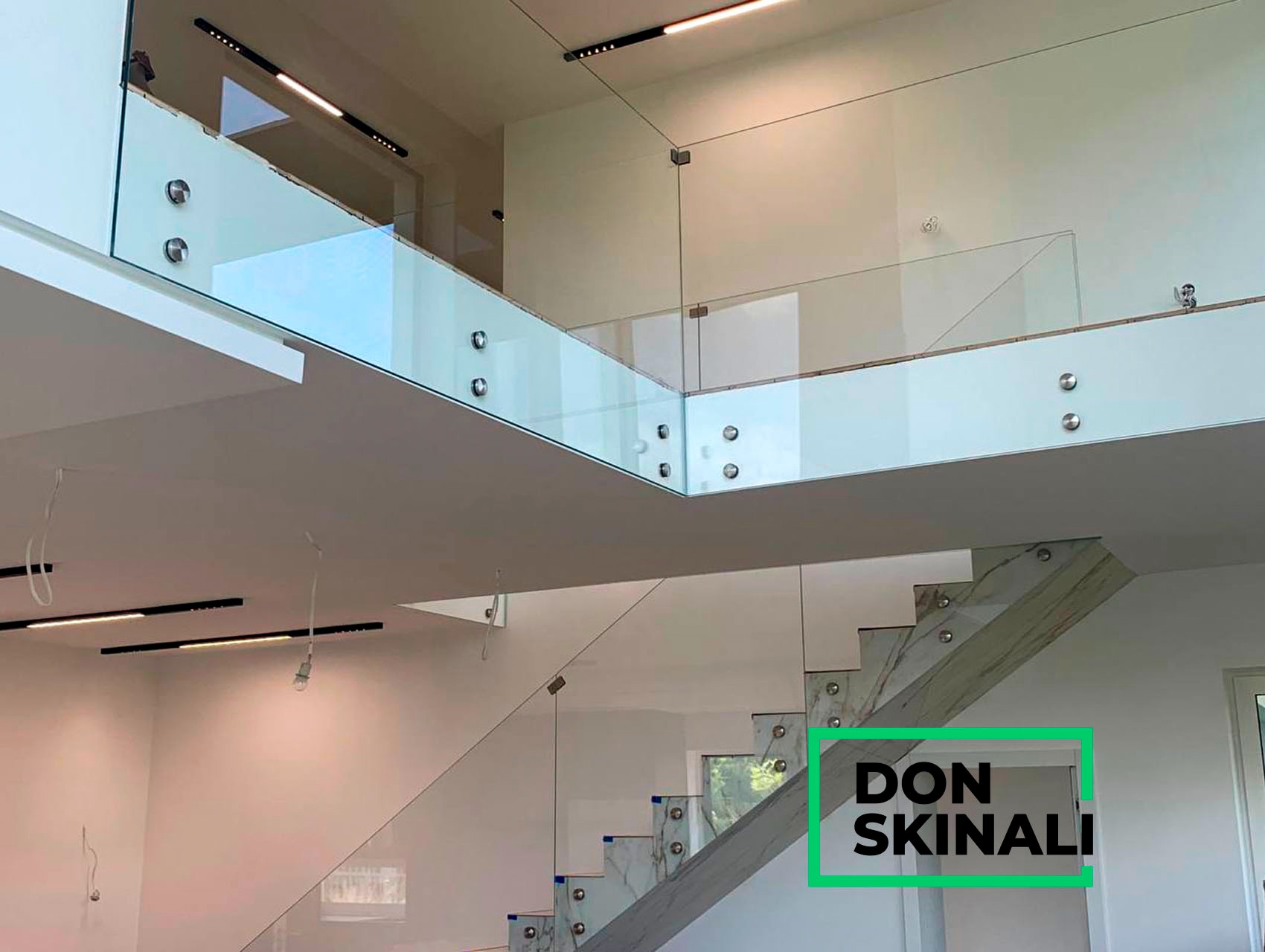 Wnętrze domu z nowoczesnymi schodami z marmurowymi stopniami i szklaną balustradą na dwóch poziomach, mocowaną za pomocą metalowych uchwytów punktowych, oświetlenie ledowe w suficie.