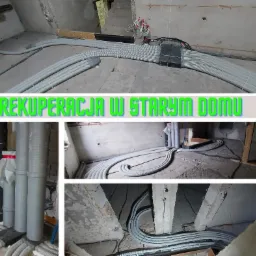 Wnętrze w trakcie prac instalacyjnych: szare, karbowane rury prowadzone po podłodze i wzdłuż ścian w surowym stanie. Widoczne przewody elektryczne i fragmenty konstrukcji budynku.