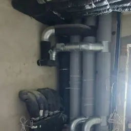 Szare i srebrne rury wentylacyjne z izolacją termiczną w surowym wnętrzu podczas montażu.