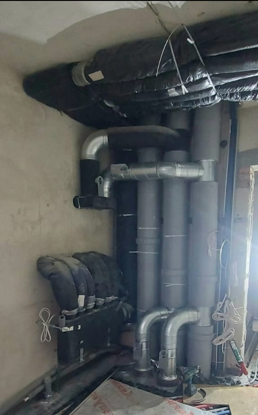 Szare i srebrne rury wentylacyjne z izolacją termiczną w surowym wnętrzu podczas montażu.