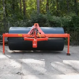 Walec rolniczy, pomarańczowa rama, czarny cylinder, tło zalesione.