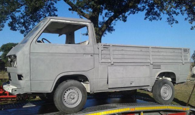 Volkswagen Transporter T3 w wersji pickup, przygotowany do lakierowania, z widocznymi śladami po usunięciu rdzy i starej powłoki, umieszczony na platformie warsztatowej na zewnątrz.