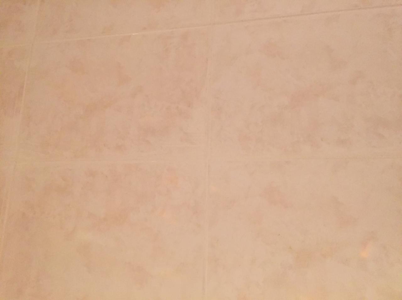 Beżowe, kwadratowe płytki ceramiczne z delikatnym wzorem, ułożone w regularną siatkę z widocznymi fugami.