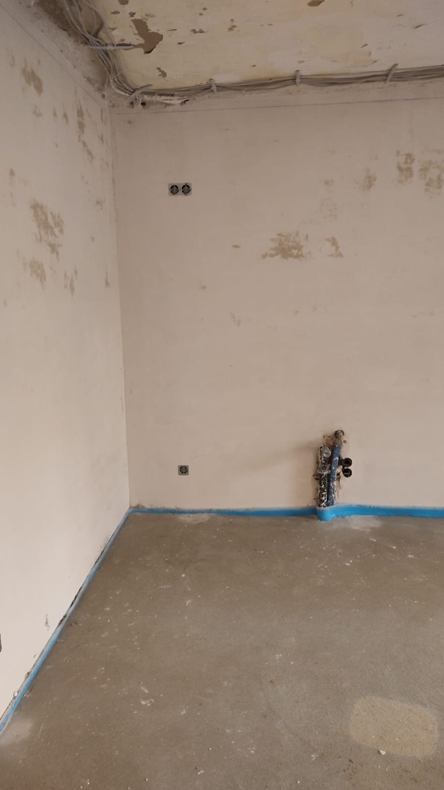 Wnętrze w trakcie remontu: widoczne przewody elektryczne pod sufitem, gniazdka w ścianie, instalacja hydrauliczna przy podłodze zabezpieczonej niebieską folią.
