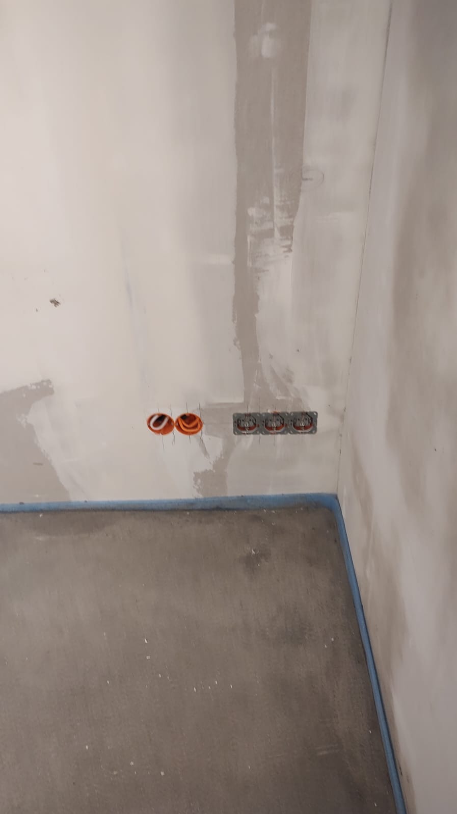 Ściana w trakcie prac wykończeniowych z zamontowanymi puszkami elektrycznymi i przewodami. Widoczne ślady po szpachlowaniu i przygotowaniu do malowania.