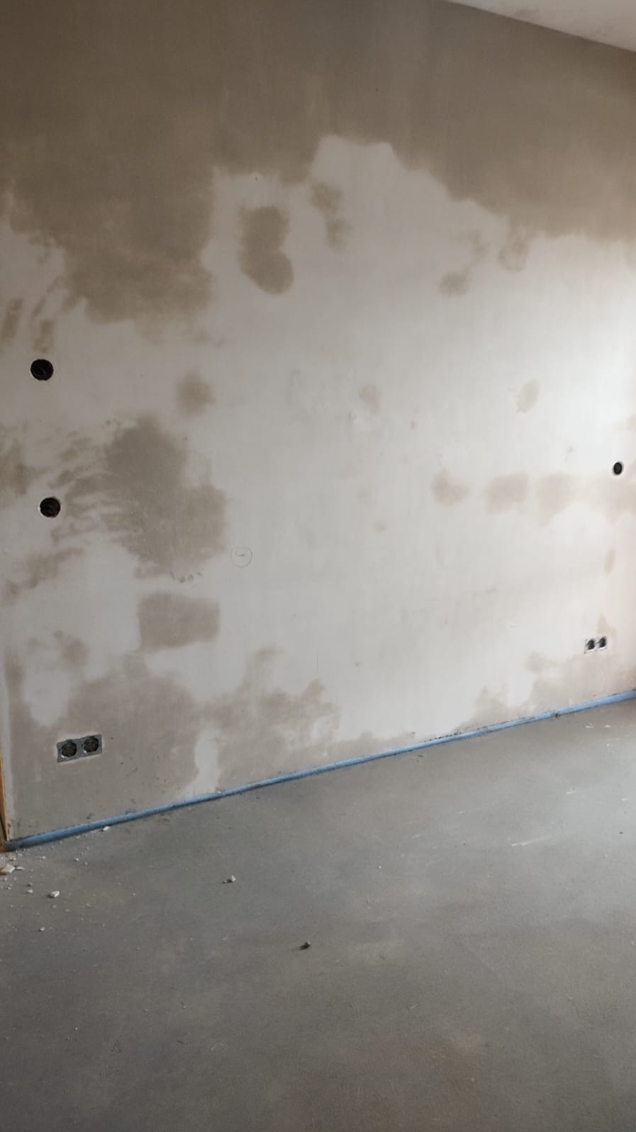 Ściana po gruntowaniu z widocznymi puszkami elektrycznymi i gniazdkami. Podłoga wylewka. Przygotowanie do dalszych prac wykończeniowych.