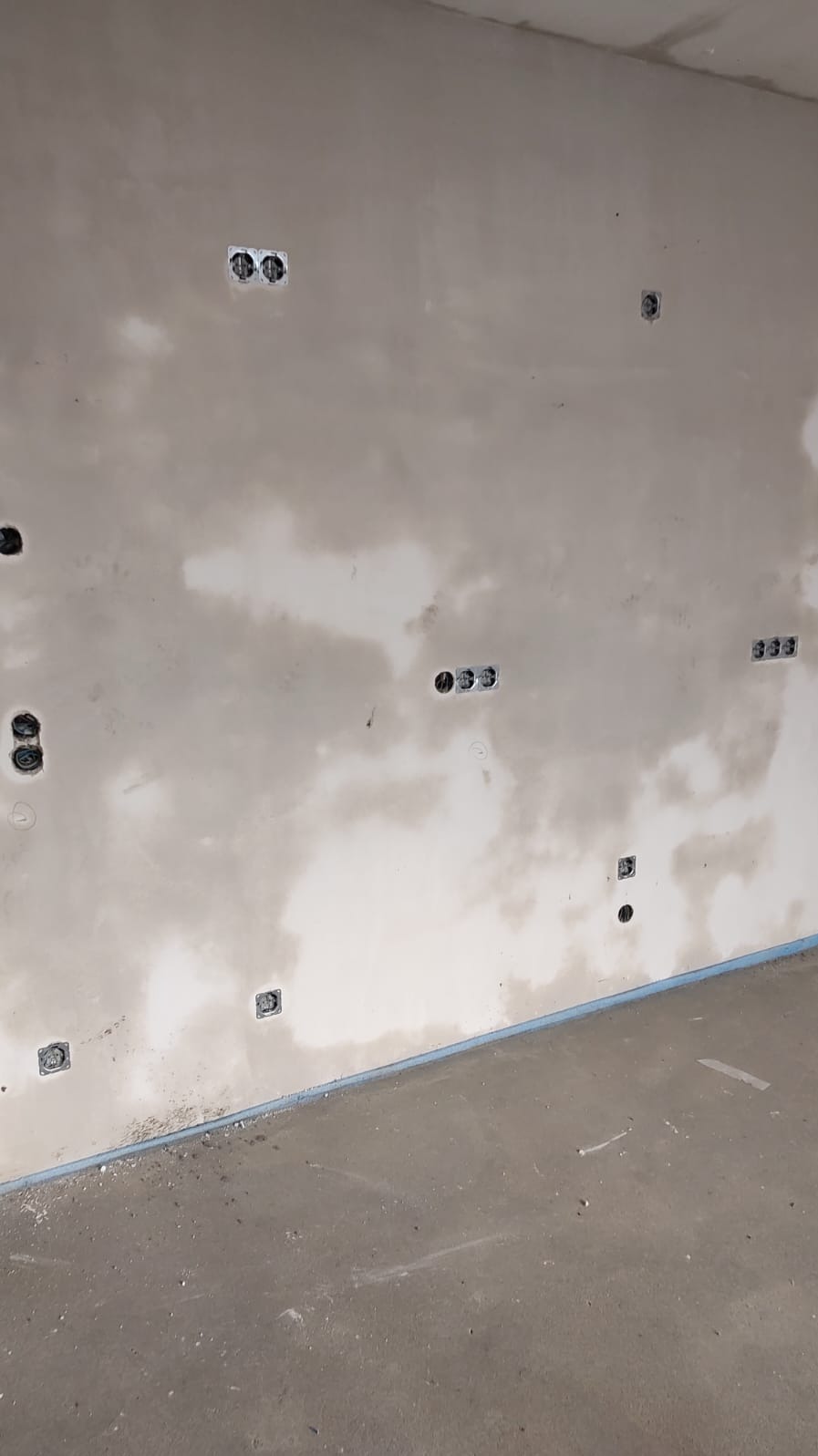 Ściana w trakcie prac instalacyjnych w Kostrzynie nad Odrą, z widocznymi puszkami elektrycznymi przed montażem gniazdek i włączników, surowy tynk.