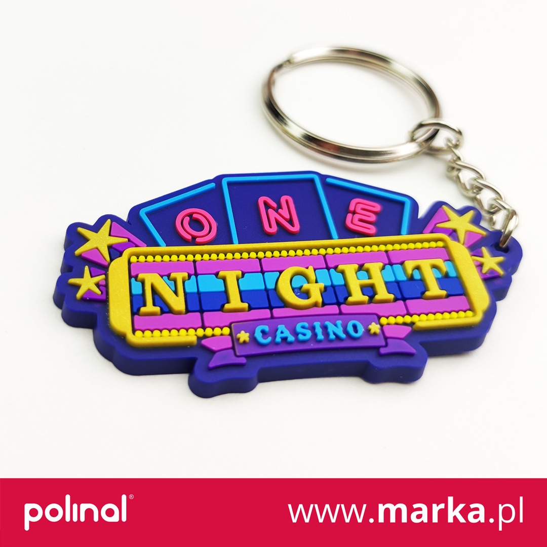 Kolorowy, gumowy brelok z napisem 'ONE NIGHT CASINO' na białym tle, z metalowym kółkiem i łańcuszkiem.