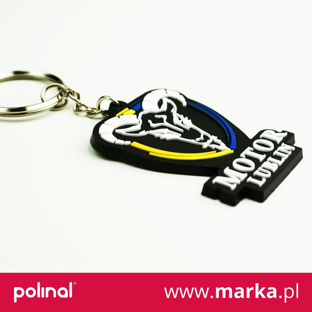 Gumowy brelok z logo Motor Lublin w kształcie głowy barana na białym tle, przymocowany do metalowego kółka.