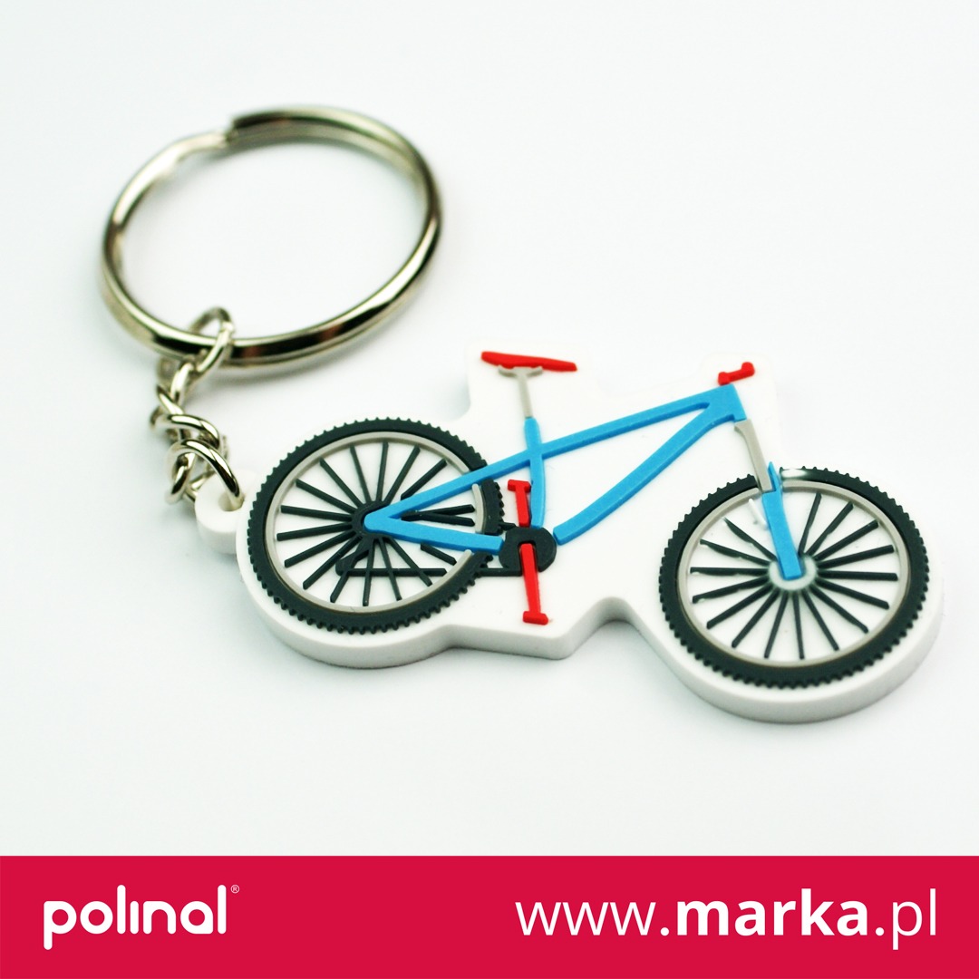 Brelok w kształcie roweru górskiego z niebieską ramą, czerwonymi elementami i czarnymi kołami na białym tle.
