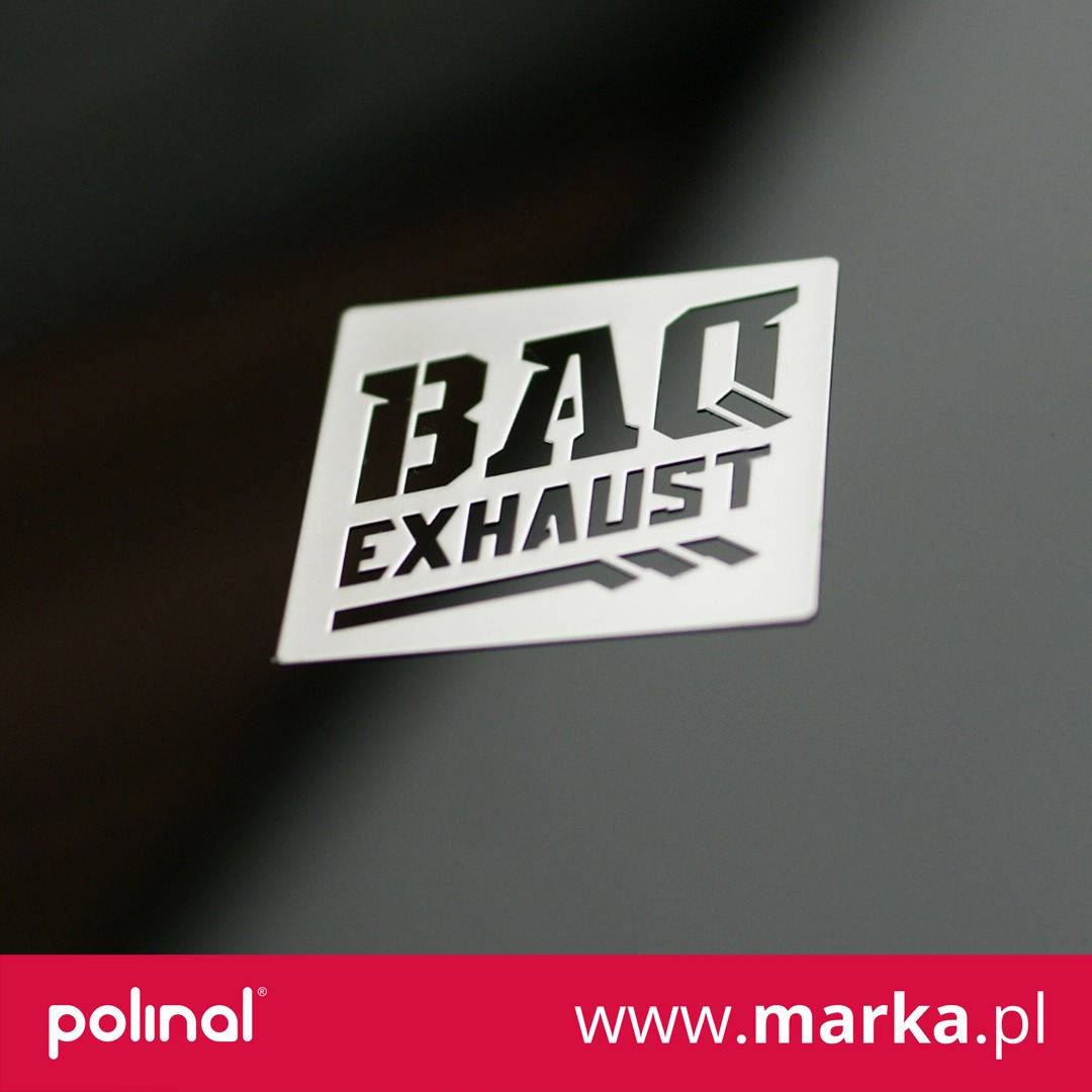 Biała, kwadratowa nalepka z czarnym logo 'BAG EXHAUST' na ciemnoszarym tle, oświetlona z góry.