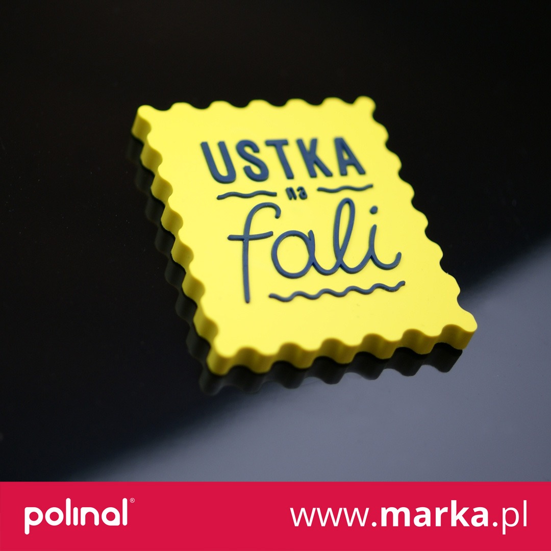Żółty, dekoracyjny magnes na lodówkę w kształcie znaczka pocztowego z napisem 'Ustka na fali' na błyszczącym, czarnym tle.