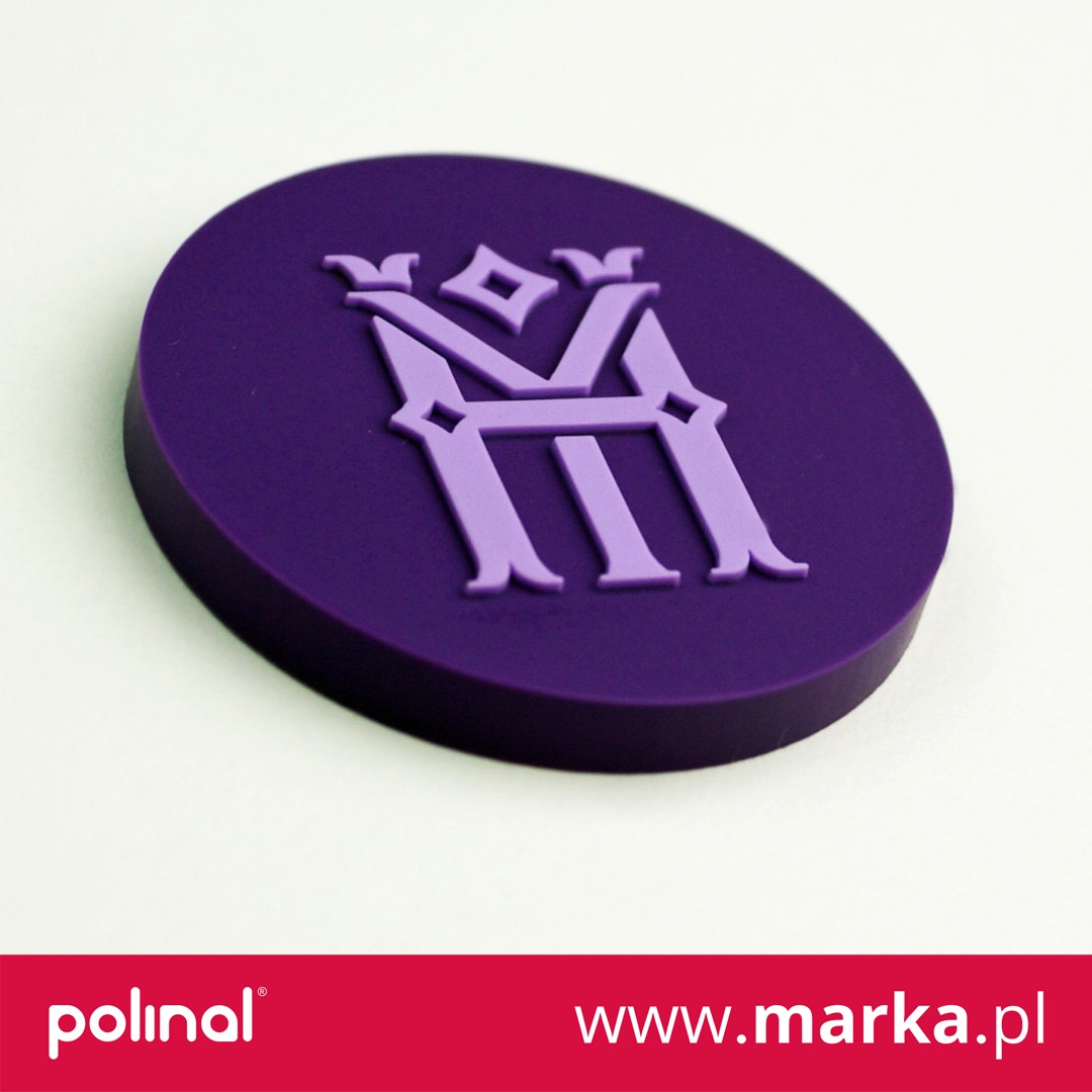 Fioletowa okrągła naklejka z wytłoczonym logo firmy w odcieniach fioletu, leżąca na białym tle pod kątem.