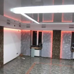 Nowoczesne wnętrze po remoncie z podświetleniem LED, marmurową posadzką, panelami ściennymi imitującymi marmur, białą cegłą i błyszczącym sufitem podwieszanym.