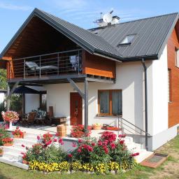 Porin - Nowoczesny dom z szarą blachodachówką, drewnianą elewacją i balkonem z metalową balustradą, otoczony ogrodem z kwiatami.