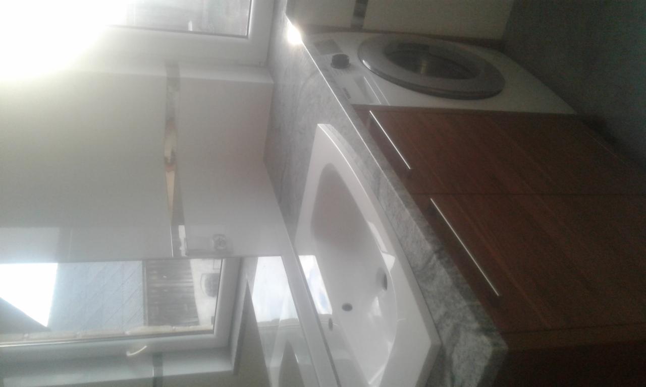 Łazienka z umywalką wpuszczoną w szary blat, obok pralka i szafka z drewnianymi frontami, widok z góry.