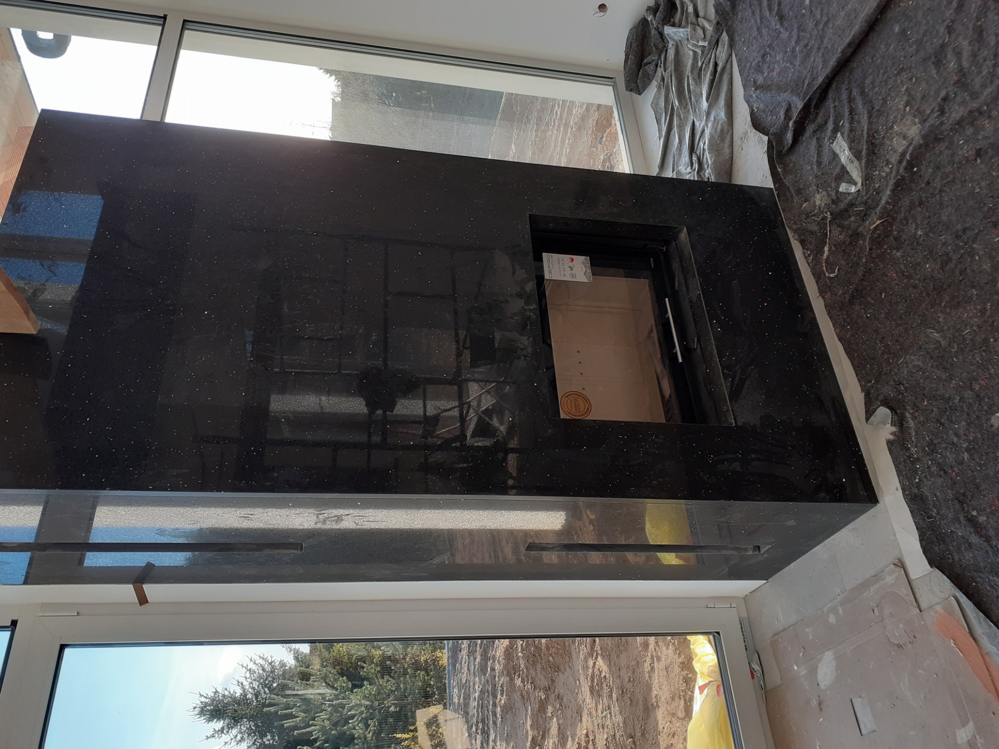 Czarny, błyszczący blat z wycięciem na zlew, zamontowany przy oknie w trakcie prac wykończeniowych, widoczne zabezpieczenia podłogi.