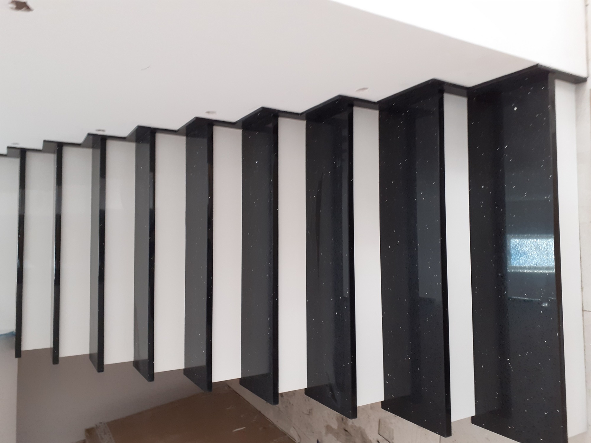 Nowoczesne schody z czarnego, błyszczącego kamienia z białymi elementami, widok z góry, surowe wykończenie.